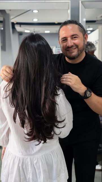 Estilista de The Salon sonriendo junto a una clienta de cabello largo
